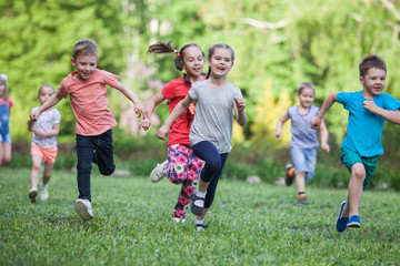 A group of happy children of boys and girls run in the Park on the grass on a Sunny summer day . The concept of ethnic friendship, peace, kindness, childhood. - Powered by Adobe