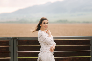 Obraz premium Attractive young girl stand outside in the village, Background of mountains. Bright photo. White clothes