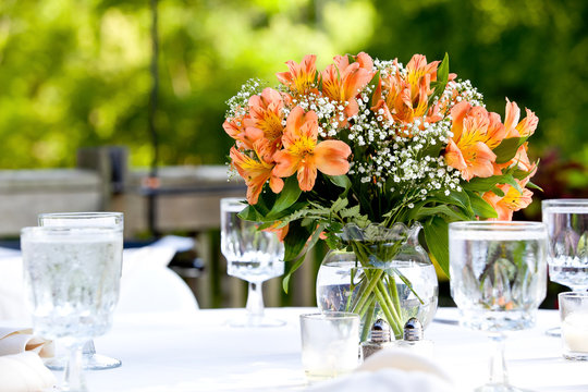 Orange bouquet of flowers on a table in clear jars of water during a wedding celebration 