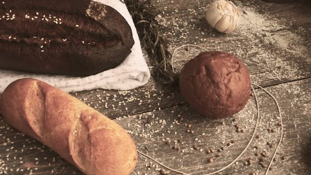 Different types of bread on wooden table dusted with flour. Slow pan.	Concept of natural food and organic food.