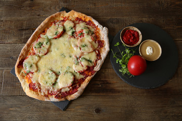 pizza with tomatoes, cheese, herbs and tomato sauce in a bowl on a wooden rustic background with copy space for text.