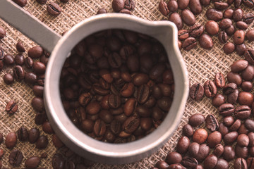 Cup with natural brown roasted coffee beans on burlap fabric background.