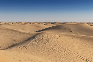 Photograph of Abu Dhabi desert with car tires marks in the sand.