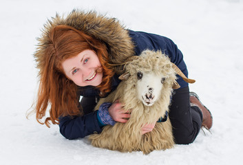 redhead woman playing with a sheep in the snow