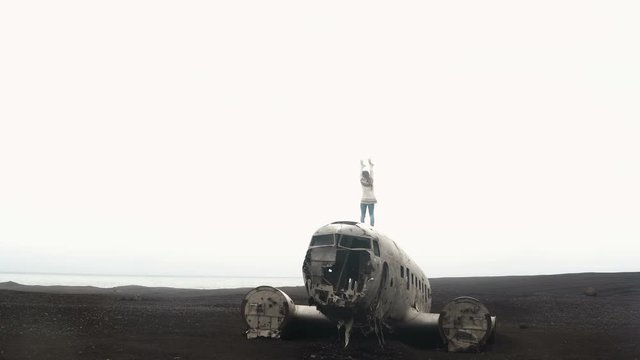 Freedom: back view of young woman in lopapeysa standing on the top of breaker DC-3 BMC plane on black beach in Iceland.
