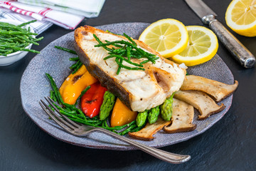 Grilled halibut steak with vegetables - sweet mini peppers, courgette, asparagus and oyster mushrooms, garnished with samphire