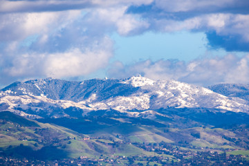 Fototapeta na wymiar View towards Mt Hamilton and the Lick Observatory building on a sunny winter day; green hills in the foreground and snow covered peaks in the background; San Jose, south San Francisco bay, California