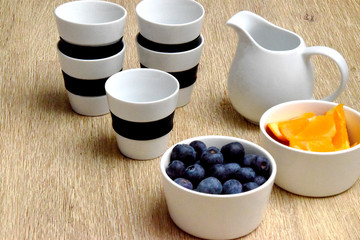 Cups, milk pot and bowls with healthy blueberries and oranges