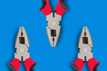 Three new metal pliers with rubber handles black and red color on blue table with copy space for...