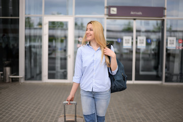 Young blonde hair business woman in shirt and denim pants standing near arrival terminal at the airport