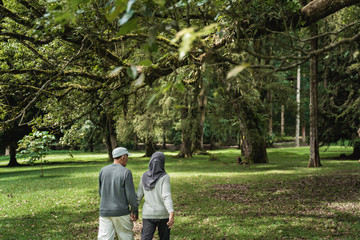 portrait of asian muslim senior couple walking in the garden together. shoot from behind