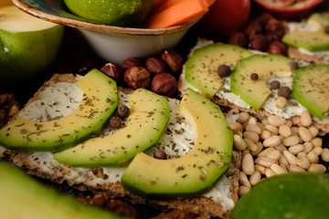 Crispbread with cheese and avocado, tomatoes, nuts, fruits, salad, spices on dark board background top view. Food and Health