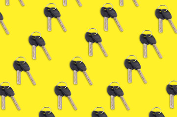 Diagonal rows of metal shiny keys with black plastic or rubber handle attached of keyring for door or car on yellow background