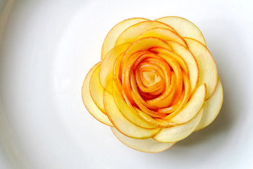 Rose carved from apple, on white porcelain - top view close up, selective focusing