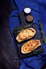Stuffed eggplant halves roasted with cheese on a black cutting board