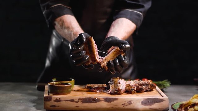 Male hands in black rubber gloves tears apart tasty roasted ribs close up. Slow motion.