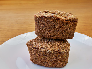 two small loaves of wheat homemade bread lie one on another on a white plate on a wooden table