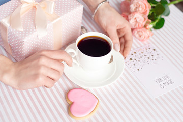 Mother's day concept - a gift for women hands with a white cup of coffee and roses. Copy space.