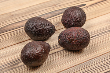 Four dark brown ripe avocados on wooden boards.