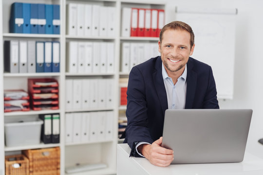 Smiling businessman sitting in office with laptop