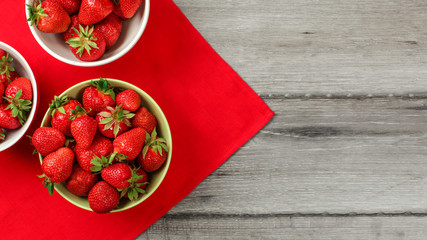 Top down view, small bowls with strawberries, red tablecloth and gray wood desk under. Space for...