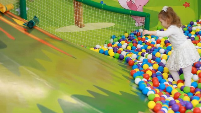 Happy child girl playing on the playground with fun. Happy childhood. Multicolored balls.