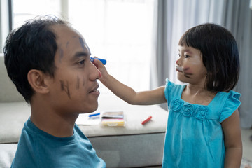 happy daughter painting on her dad's face at home