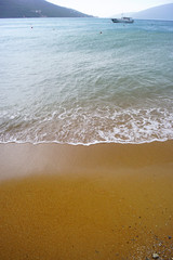 The view from the sandy beach of the sea in the bay with a small boat on the horizon.