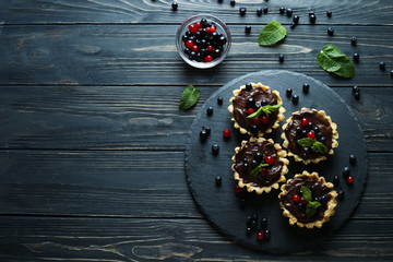 Delicious juicy berry cakes with chocolate cream on dark wooden background. Top view with text space