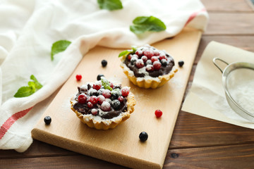 Delicious juicy berry cakes with chocolate cream on wooden background. Side view
