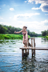 Little cute girl jumping off the dock into a beautiful river at sunset
