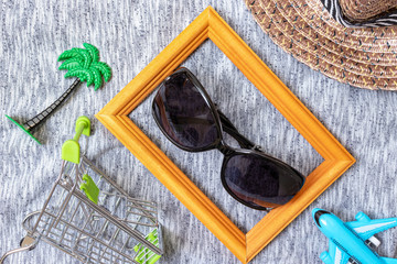 Shopping cart, straw hat, plane and sunglasses on textile background, flat lay - shopping tourism concept