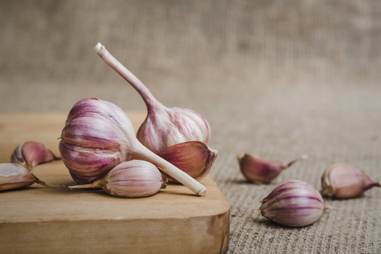 Bulbs and cloves of natural organic farm garlic on a wooden cutting board against a background of linen matting
