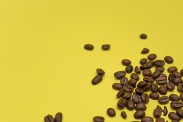 Coffee beans randomly scattered in right-down corner of  yellow background.