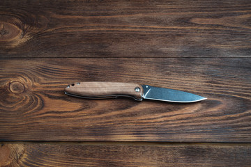 hunting bowie knife with a wooden handle on dark wooden background. Steel arms weapon. top view