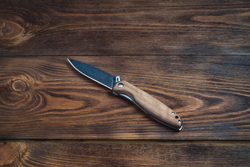 hunting bowie knife with a wooden handle on dark wooden background. Steel arms weapon.