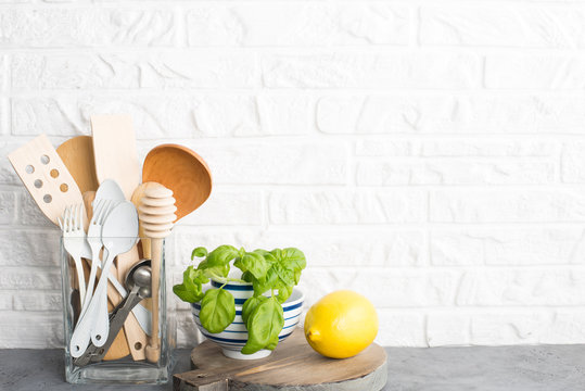 Kitchen tools, olive cutting boan a kitchen shelf against a white brick wall. Fresh basil and lemon. White and black modern cutlery. No plastic house