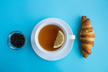 Tea time.Cup of hot black tea and croissant on the blue  background.Top view.Copy space.