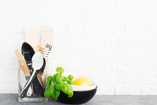 Kitchen tools, olive cutting boan a kitchen shelf against a white brick wall. Fresh basil and lemon. White and black modern cutlery. No plastic house