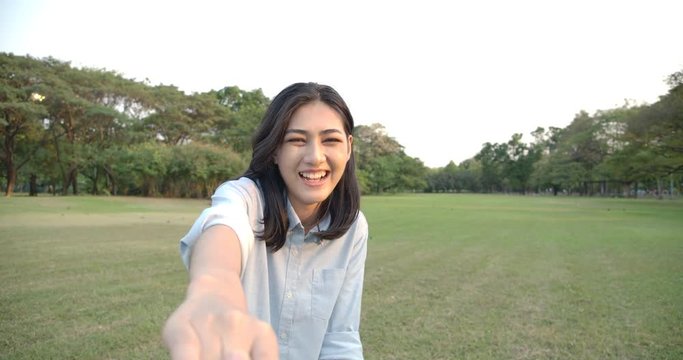 POINT OF VIEW: Young attractive asian woman pulling her boyfriend through a summer Park at sunset. SLOW MOTION. POV: Happy girlfriend makes her man to follow her in the park.