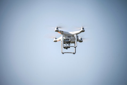 White observation drone is flying high in the clear blue sky