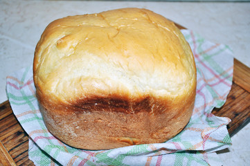 Homemade white bread baked in a bread maker with a crispy crust, cut with a knife.