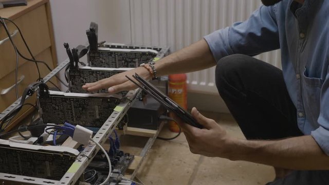 Young engineer monitoring temperature and checking connection on a cryptocurrency mining rig using software on pc tablet