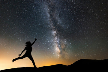 Beautiful starry night, female silhouette jumping on the milky way background. Night landscape. with milky way galaxy.