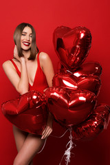 Young beautiful brunette woman with a sweet white smile in red lingerie and a balloon in the form of heart in his hands on a  red background