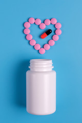 Heart of pink pills, tablets and white bottle on blue background.