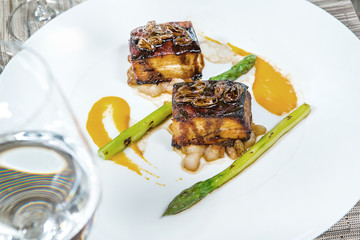 fried eel on a white plate with asparagus and soy sauce, glass of wine in the foreground
