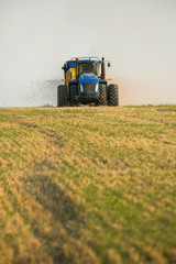 Obraz premium the tractor fertilizes the field with manure. A large trailer. Sowing. Agroindustry.Pole before sowing. Against the sky. yellow tractor.