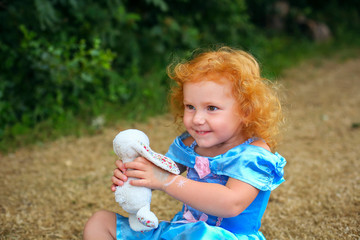 Portrait of cute little redhead girl in blue dress walking in park and playing on party for children in sunny day