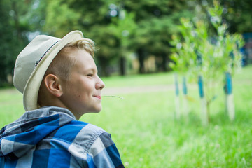 Lovely young guy wearing hat having a rest in a park. Laughing kid boy 12-16 year old outdoors. Childhood. Schoolboy. Summer.